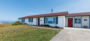 A two-story building with a red door and windows, a small garden with yellow flowers, and a clear sky. - Point Arena Lighthouse - Keeper's Apartment (Point Arena)