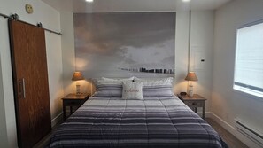 Une chambre à coucher avec un lit, deux tables de chevet avec des lampes, une armoire en bois et une fresque murale représentant un paysage urbain.