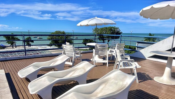 Eine Terrasse mit Liegestühlen und Sonnenschirmen mit Blick auf einen Strand.