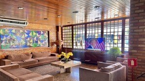 Eine großzügige Lobby mit einem großen Fernseher, der Nachrichten zeigt, einem gemütlichen Sitzbereich mit Sofas, einem Couchtisch und einem großen Fenster mit Blick nach außen.