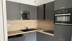 A compact kitchen with grey cabinets, a black microwave, a built-in oven, and a dishwasher. - 150m from ski slopes, 1st floor, view ski slopes, swimming pool, balcony, tv, ski locker, 58m² (Eaux-Bonnes)