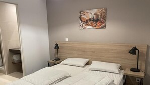A neatly made bed with white bedding and pillows, a wooden headboard, a wall-mounted artwork depicting autumn harvest, and a small bedside table with a lamp. - 150m from ski slopes, 1st floor, view ski slopes, swimming pool, balcony, tv, ski locker, 58m² (Eaux-Bonnes)