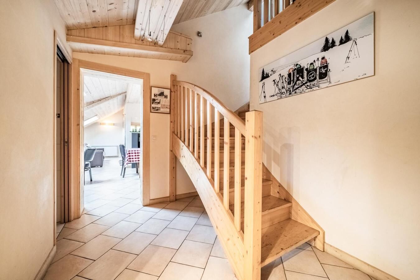 A wooden staircase leading to a second floor, a tiled floor, and a wall with a framed picture.