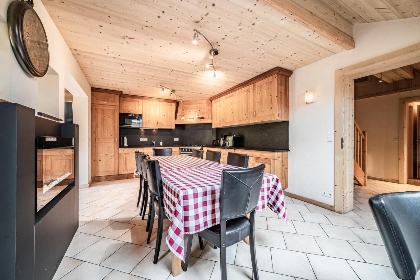 Een keuken met houten kastjes, een eettafel met geruit tafelkleed en een zwarte koelkast.