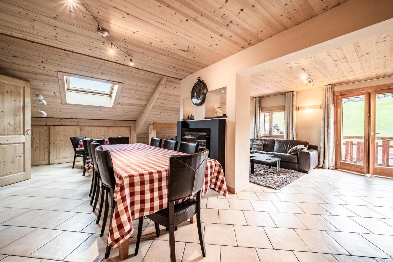 Une salle à manger spacieuse avec une nappe à carreaux, une cheminée et un salon confortable doté d’un canapé et offrant une vue sur l’extérieur.