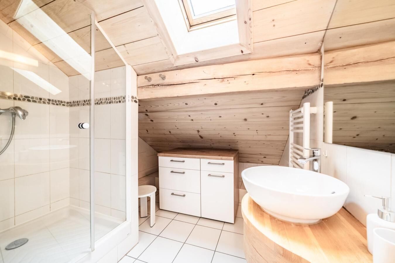 Une salle de bain avec un puits de lumière, une douche, un lavabo et un meuble de rangement.