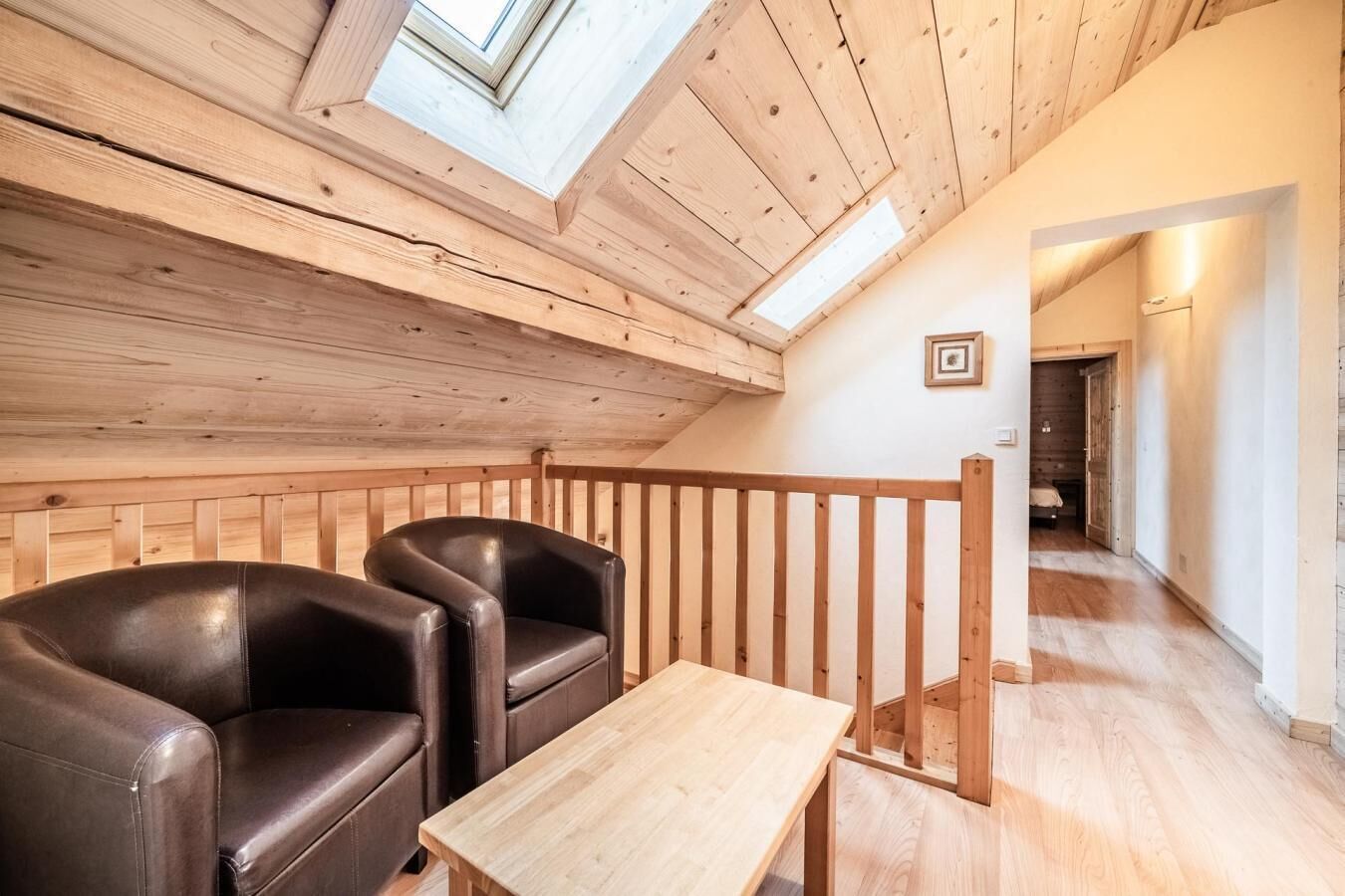 A cozy room with a wooden ceiling, two leather chairs, a small table, and a wooden railing.