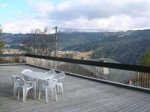 Eine Holzterrasse mit Tisch und Stühlen mit Blick auf ein Tal mit Häusern und Bäumen.