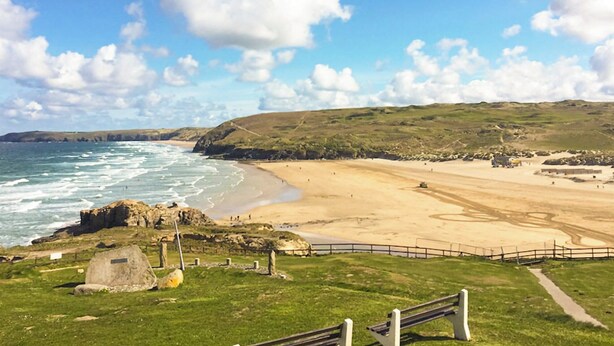 Paisagem costeira com praia, áreas gramadas e afloramentos rochosos.