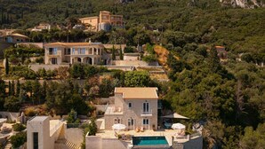 Une propriété située sur une colline, comprenant plusieurs bâtiments, dont une imposante maison en pierre dotée d’une piscine.