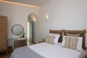 Ein Schlafzimmer mit einem großen Bett, einem hölzernen Kopfteil, einem runden Spiegel und einem kleinen Tisch mit einer Vase.