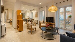Un vaste espace de vie comprenant une table à manger, des chaises, un canapé et un téléviseur. Une grande fenêtre offre une vue sur l’extérieur.