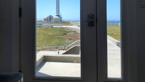 Une pièce avec une porte donnant sur une vue d’un phare et d’une zone herbeuse.
