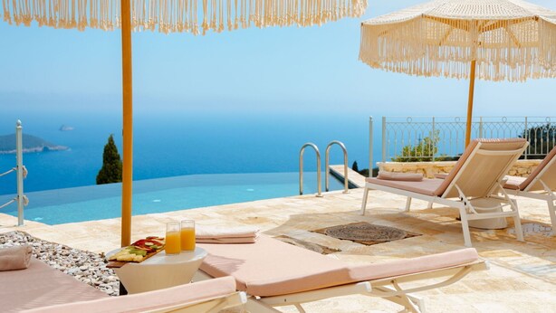 A poolside area with lounge chairs, a table with drinks, and a view of the sea.