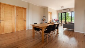 Una habitación amplia con una mesa de comedor de madera, sillas negras, un sofá gris y un gran ventanal con vistas a la vegetación.