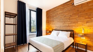Habitación de hotel moderna con una pared de madera, una cama grande, una mesita de noche con lámpara y una ventana con cortinas.