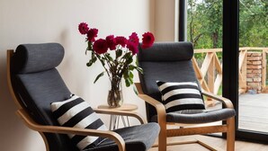 Dos sillones modernos con cojines a rayas negras y blancas, un jarrón con flores rojas y vista a una terraza de madera a través de un ventanal grande.