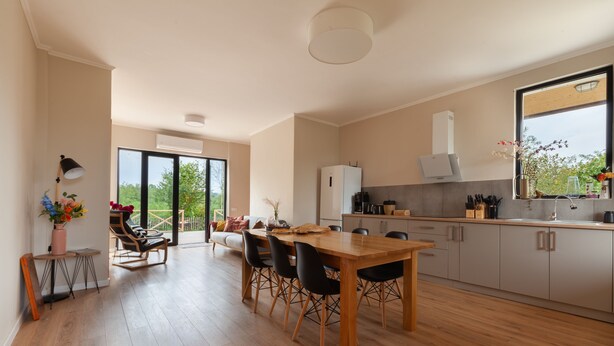 Una cocina moderna con armarios de madera, una zona de comedor con mesa y sillas de madera, y un ventanal con vistas a zonas verdes.