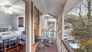 Une chambre avec un lit, une chaise et une table sur une véranda en bois dotée d’une balustrade.