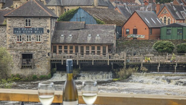 Ein Tisch mit einer Flasche und Gläsern, mit Blick auf einen Fluss und Gebäude im Hintergrund.