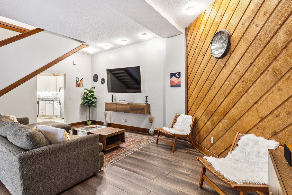 A modern living room with a sofa, a chair, a coffee table, a TV, and a wooden accent wall.