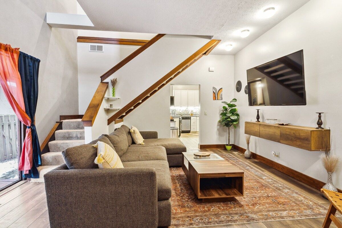 A modern living room with a staircase, a flat-screen TV, and a wooden coffee table.