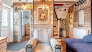 Una sala de estar acogedora con un sillón antiguo, un sofá azul y una escalera de madera.
