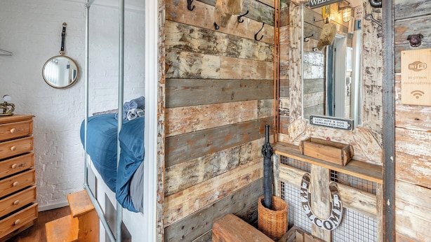 Una habitación rústica con una cama, un espejo y un letrero que dice 'Welcome'.