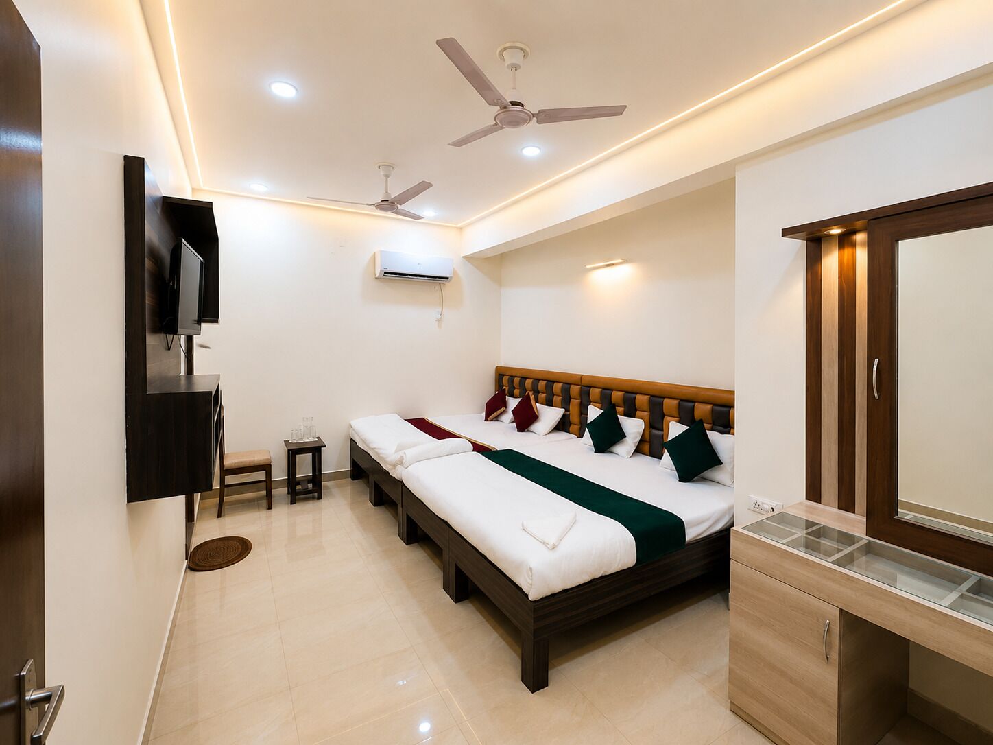 A hotel room with a bed, bedside tables, a TV, ceiling fans, and an air conditioning unit.