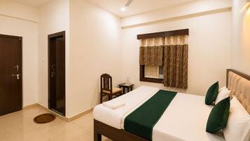 A hotel room with a bed, a chair, a desk, a window with curtains, a ceiling fan, and a door.