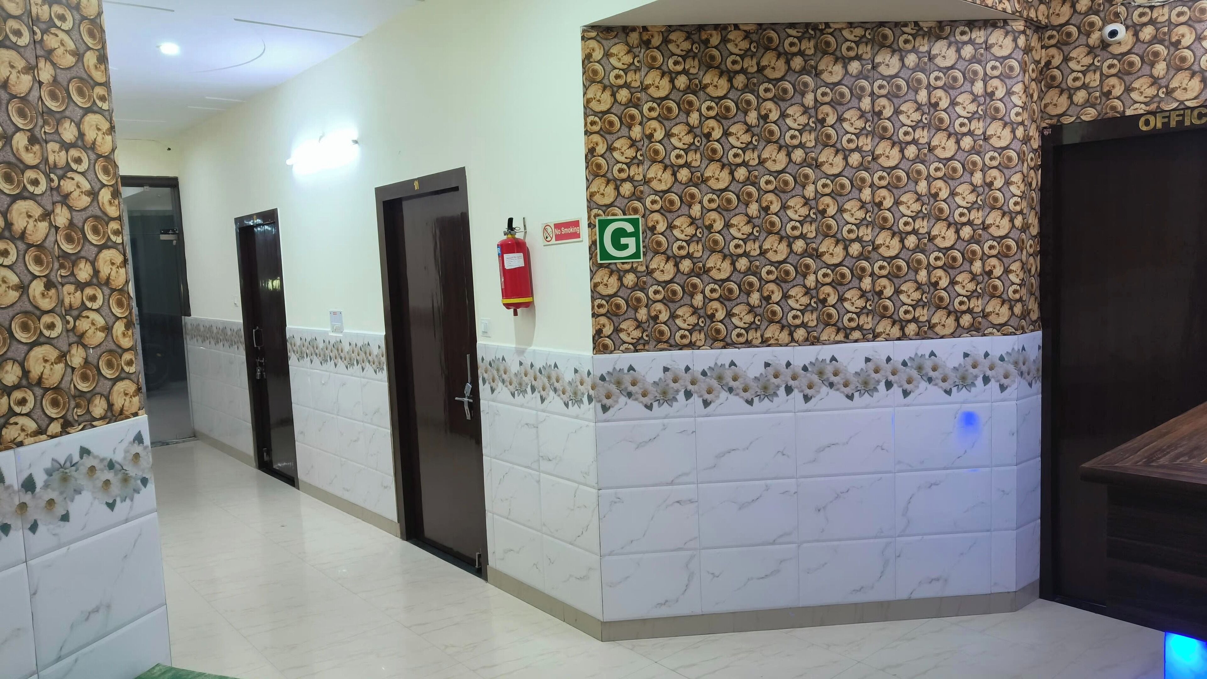 Un couloir avec un mur orné de motifs, un extincteur, un panneau « Interdiction de fumer » et un panneau vert avec la lettre « G ».