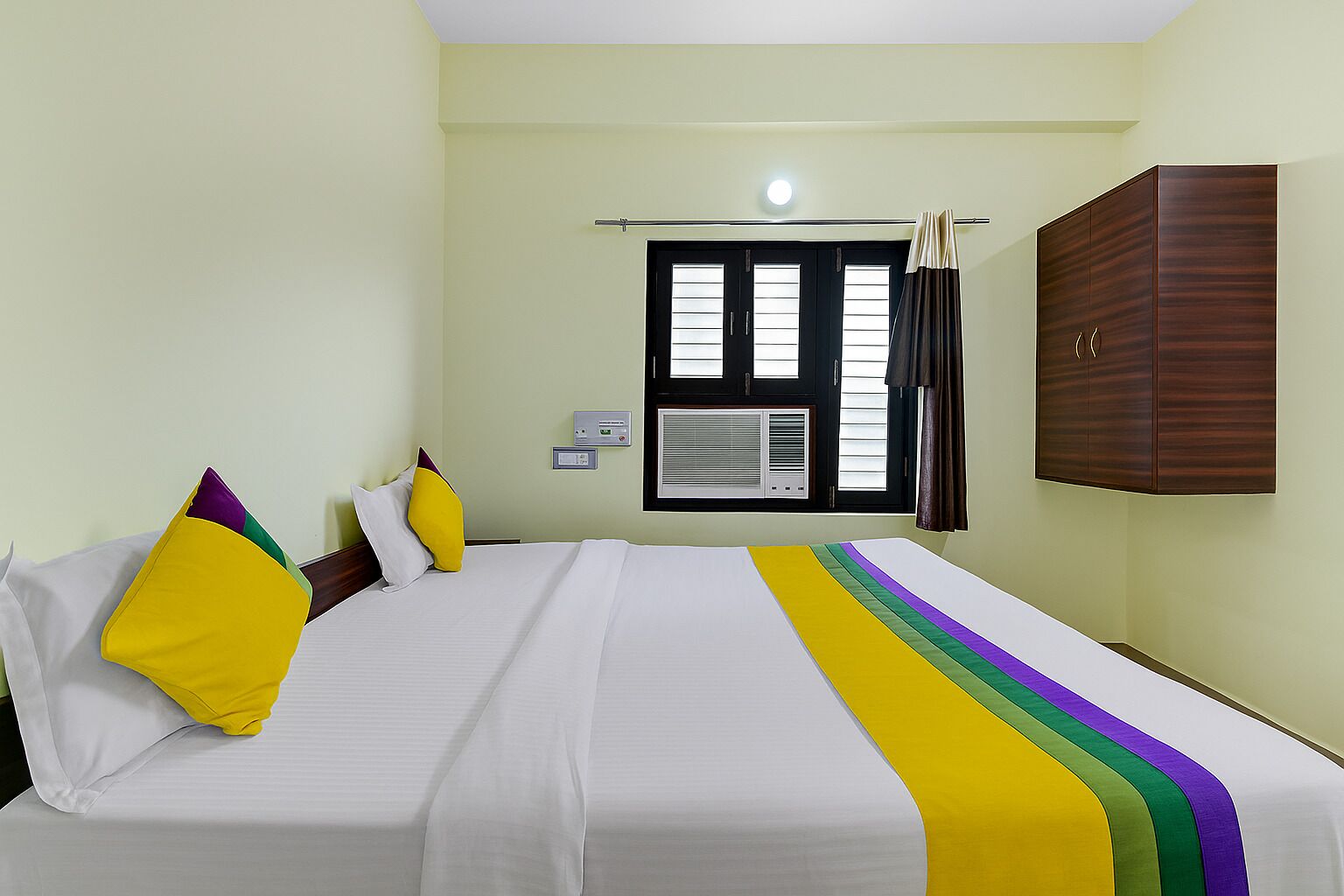 Una habitación de hotel con cama, armario, ventana con persianas y aire acondicionado.