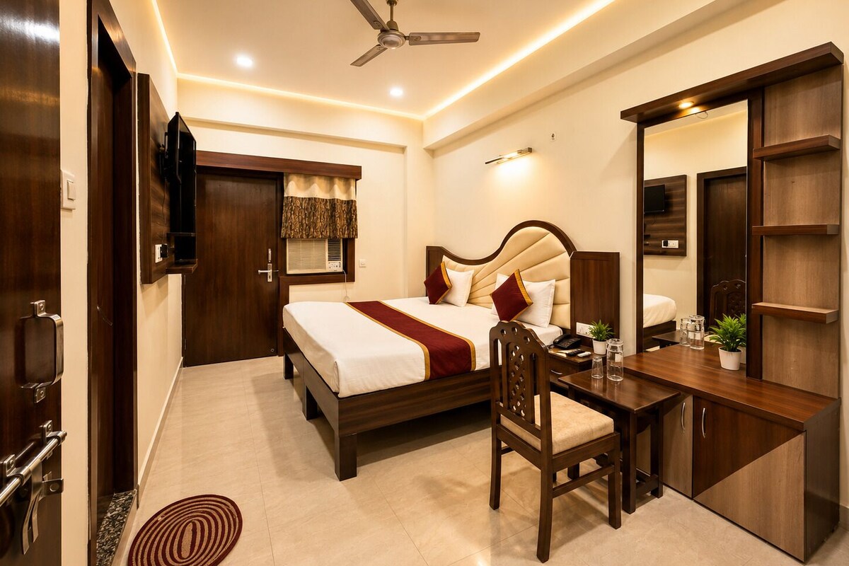 A hotel room with a bed, desk, chair, ceiling fan, and a TV mounted on the wall.