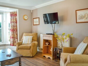 A living room with two armchairs, a wooden coffee table, a TV on a stand, a clock, and a framed picture on the wall.