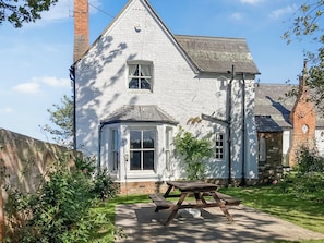 A white brick house with a small porch and a picnic table in the yard.