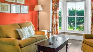 Een kamer met een bank, een tafel, een lamp en een raam met gordijnen.