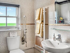 Ein Badezimmer mit Toilette, Waschbecken, Dusche mit Glastür und Fenster mit Blick zum Himmel.
