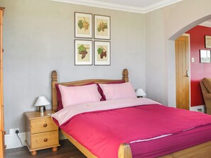 A bed with a wooden headboard, two bedside tables with lamps, and four framed botanical prints on the wall.