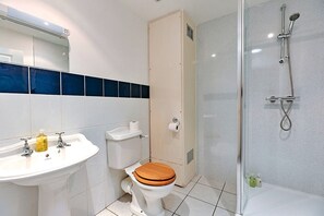 Une salle de bain avec un lavabo blanc, des toilettes en bois, une cabine de douche en verre et un mur recouvert de carreaux bleus.