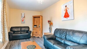 A living room with two black leather sofas, a wooden coffee table, a wooden cabinet, and a painting of a woman in a red dress. - Jasmine Country Cottage (Dorrington)