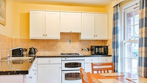 A compact kitchen with white cabinets, a black microwave, a stove, and a dining table with chairs. - Jasmine Country Cottage (Dorrington)