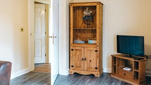 Een kamer met een houten kast, een televisie op een houten standaard, en een deur die naar een andere kamer leidt.