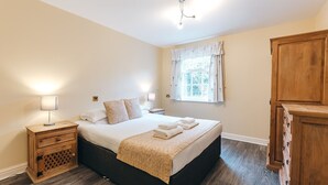 A neatly arranged bedroom with a bed, bedside lamps, a wooden nightstand, and a wardrobe. - Camelia Country Cottage (Dorrington)