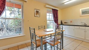 A kitchen with a dining table, chairs, a window with curtains, and a sink. - Netley Hall - Angelica (Dorrington)