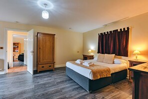 A bedroom with a large bed, wooden wardrobe, two bedside tables with lamps, and a door leading to another room.