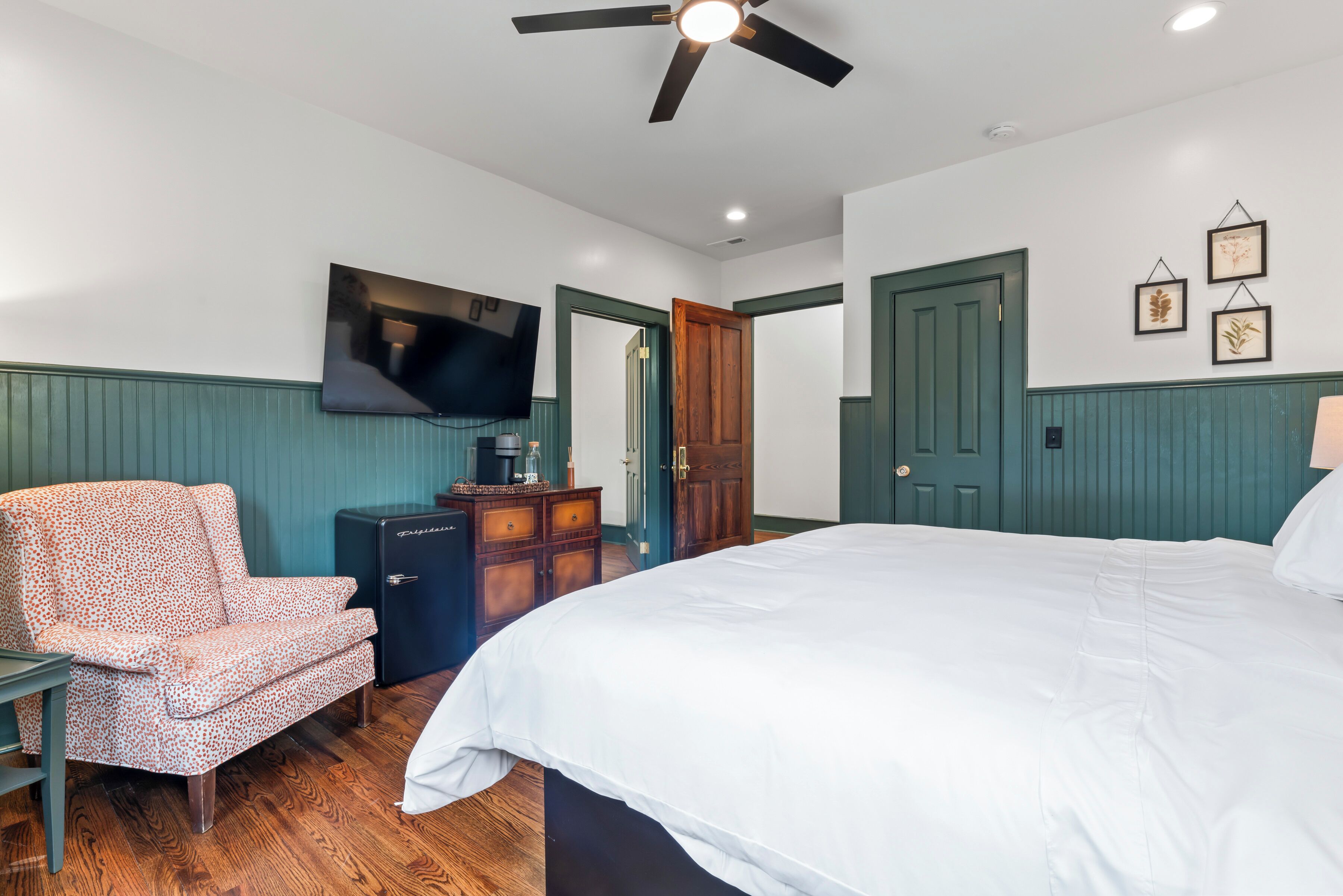 A bedroom with a bed, a chair, a dresser, a television, and a ceiling fan.