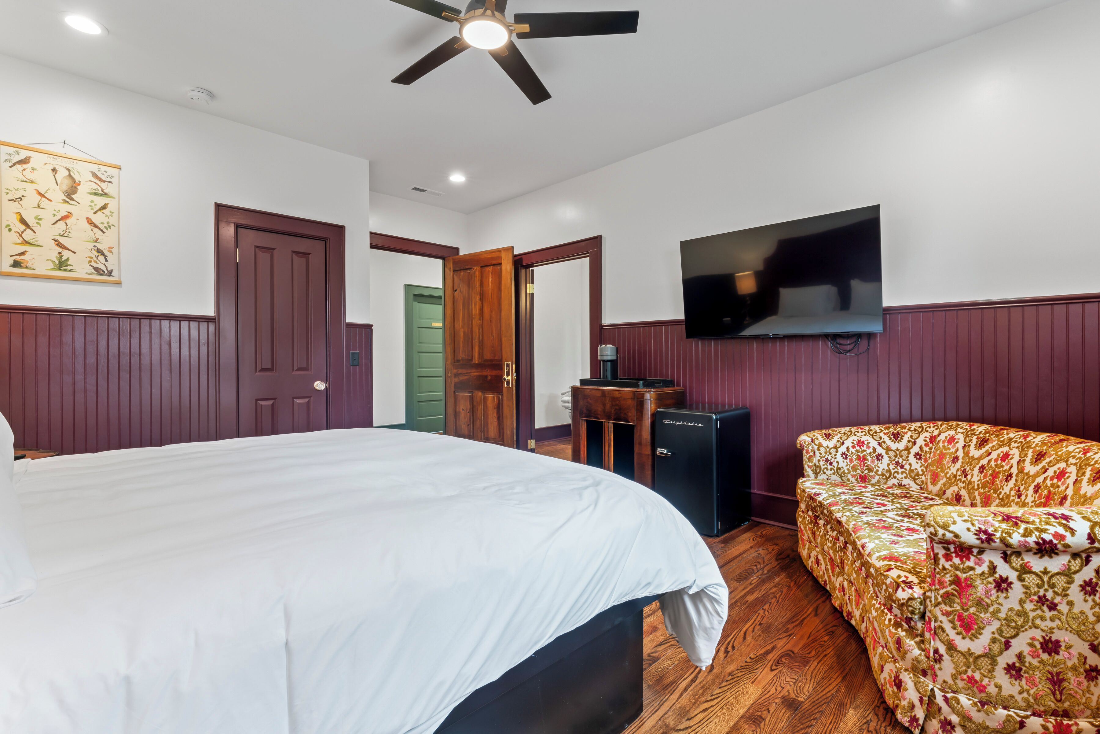 A bedroom with a bed, a sofa, a TV, and a ceiling fan.