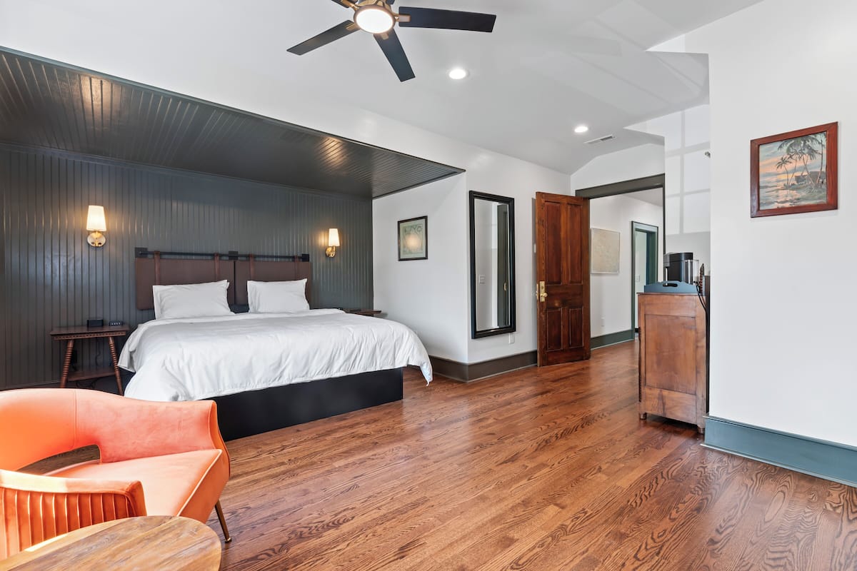 Quarto com cama, ventilador de teto, mesa de cabeceira, armário de madeira e uma cadeira.