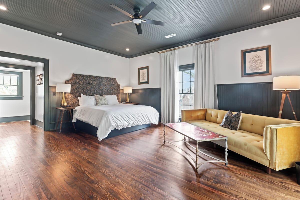 Quarto de hotel com uma cama grande, um sofá, uma mesa de centro e um ventilador de teto.