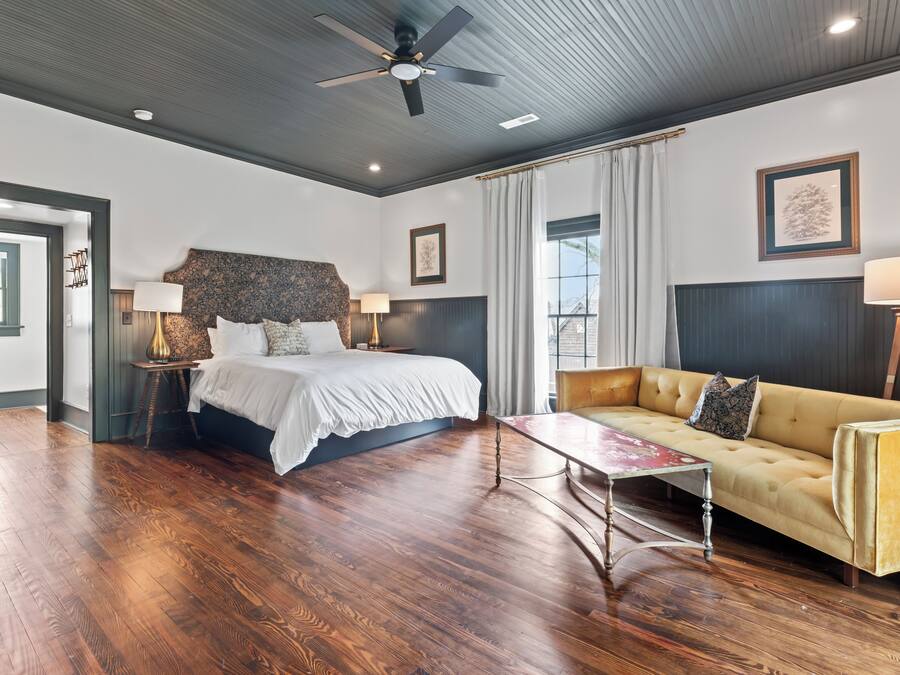 A hotel room with a large bed, a sofa, a coffee table, and a ceiling fan.